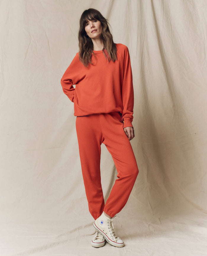 A woman stands against a beige backdrop wearing THE GREAT.’s Stadium Sweatpant in Desert Clay—an effortlessly cool, comfy look from the SU25 SEASONAL KNITS collection, perfect for the stadium or relaxing in style.