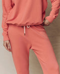 Model wearing The Stadium Sweatpant in Guava by THE GREAT. SU26 SEASONAL CORE, pairing it with a matching sweatshirt and striking an athletic pose with one hand on their hip for effortless style.