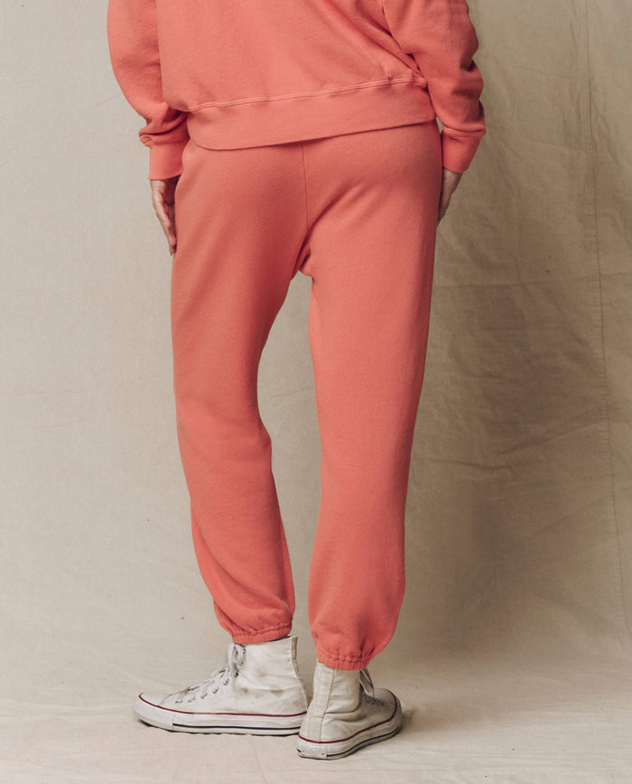 Model in The Stadium Sweatpant. Solid -- Guava by THE GREAT. SU26 SEASONAL CORE, paired with a matching sweatshirt and white high-top sneakers, stands on a neutral backdrop, showcasing relaxed athletic style from the back.