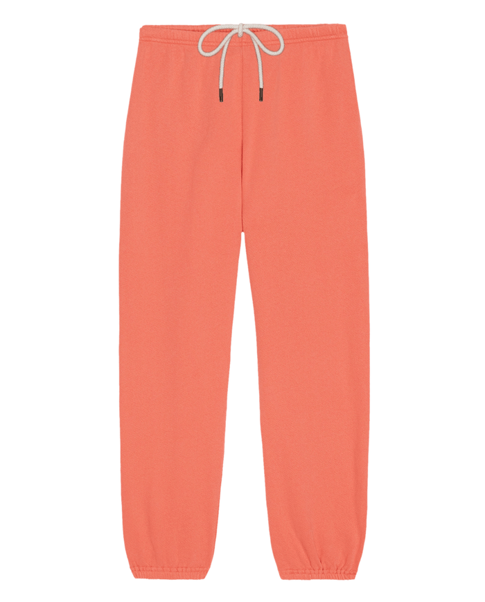 The Stadium Sweatpant. Solid -- Guava by THE GREAT. SU26 SEASONAL CORE features a coral hue, elastic waistband with white drawstring, and elastic cuffs—ideal for athletic wear or casual comfort—shown against a white background.