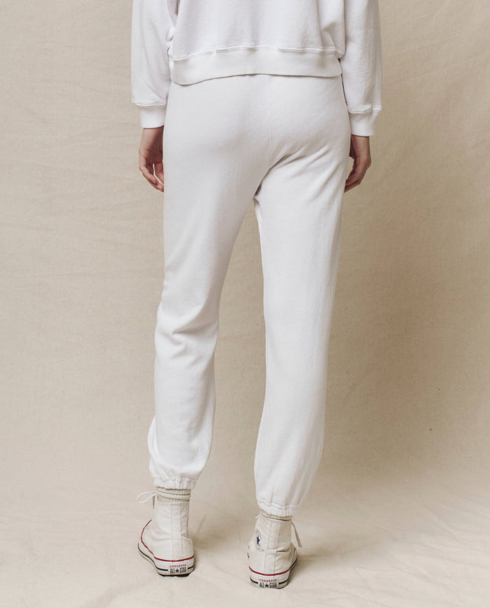 A person wearing THE GREAT. HOL 24 KNITS's The Stadium Sweatpant in True White, featuring an elasticated waist, stands with their back to the camera. The vintage athletic vibe is completed by sleek white high-top sneakers and a matching white sweatshirt.