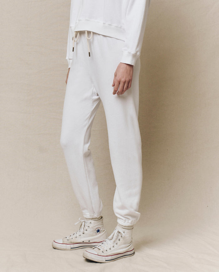 An individual wearing The Stadium Sweatpant in True White by THE GREAT. HOL 24 KNITS, paired with vintage high-top sneakers, stands against a beige background.