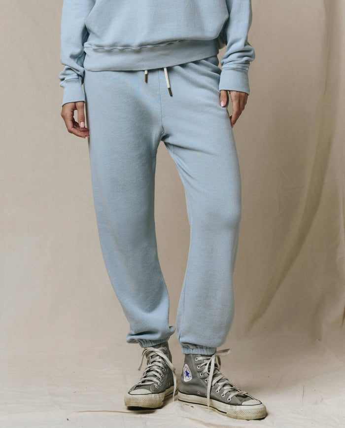 A person wears THE GREAT.’s The Stadium Sweatpant in Whisper Blue from the SP26 Seasonal Core, with matching sweatshirt and off-white high-top sneakers, standing on a neutral background. Inspired by vintage athletic wear, handcrafted in Los Angeles.