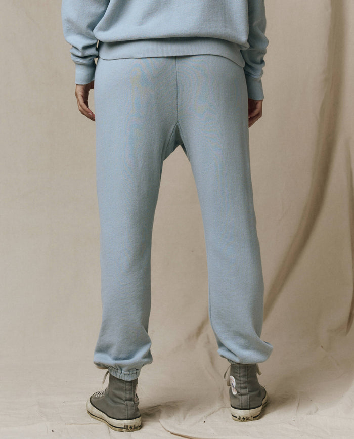 A person stands with their back to the camera, wearing THE GREAT. SP26 SEASONAL CORE The Stadium Sweatpant in Whisper Blue, a matching sweatshirt, and light-colored high-top shoes against a neutral background.
