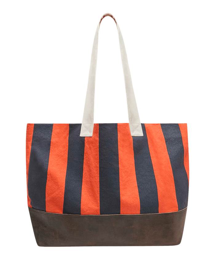 Introducing The Stripe Tote by THE GREAT. in Hot Red Prep Stripe—a large canvas tote featuring bold vertical orange and navy stripes across the top, a rich brown leather-like base, and two long white handles for easy carrying.