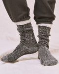A person stands on a light-colored surface wearing black THE GREAT. SP25 SWEATSHIRT SOCKS, a cozy sweatshirt, and dark pants with elastic cuffs.