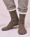 Wearing THE GREAT. CARRYOVER The Sweatshirt Sock in Chocolate with gray sweatpants, standing on a light-colored surface.