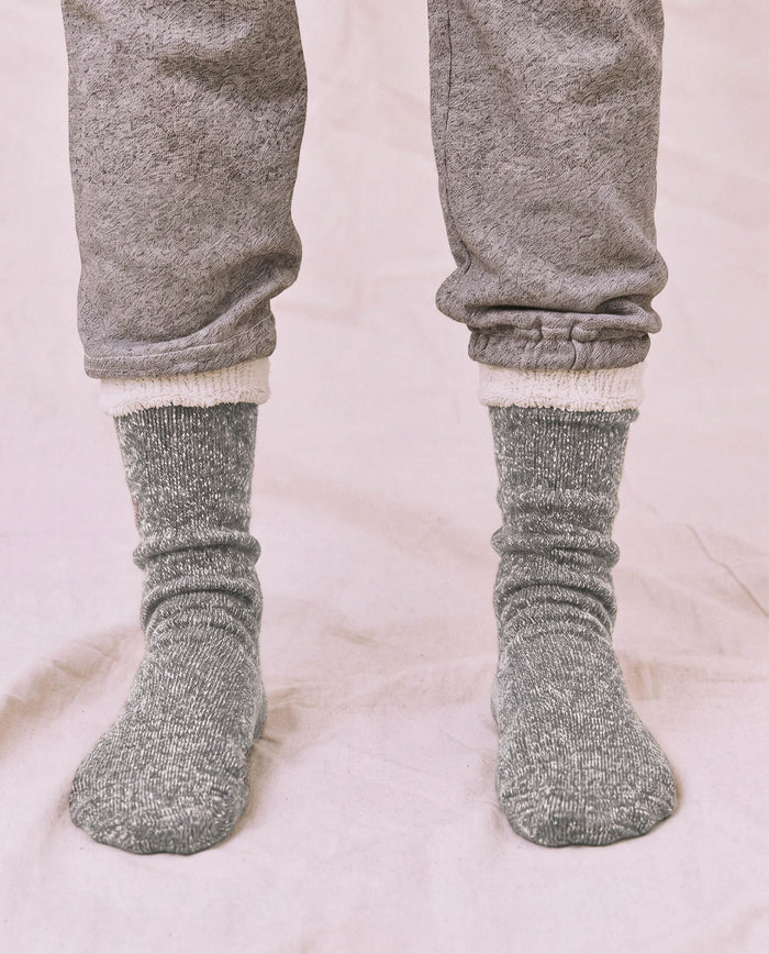 A person wears THE GREAT. CARRYOVER’s The Sweatshirt Sock in Heather Grey, standing on a light-colored surface in light gray sweatpants and thick, cozy socks.