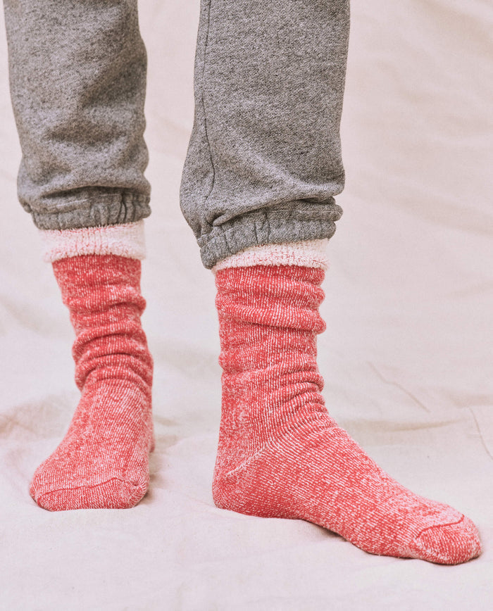 A person stands on a light fabric surface wearing gray sweatpants with a matching sweatshirt, paired with THE GREAT. SP25 SWEATSHIRT SOCKS in Red Cherry.