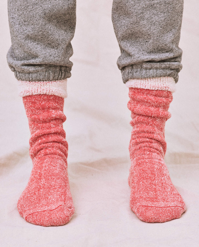 A person in a cozy gray sweatshirt with matching sweatpants and THE GREAT. SP25 SWEATSHIRT SOCKS in Red Cherry stands on a light surface.