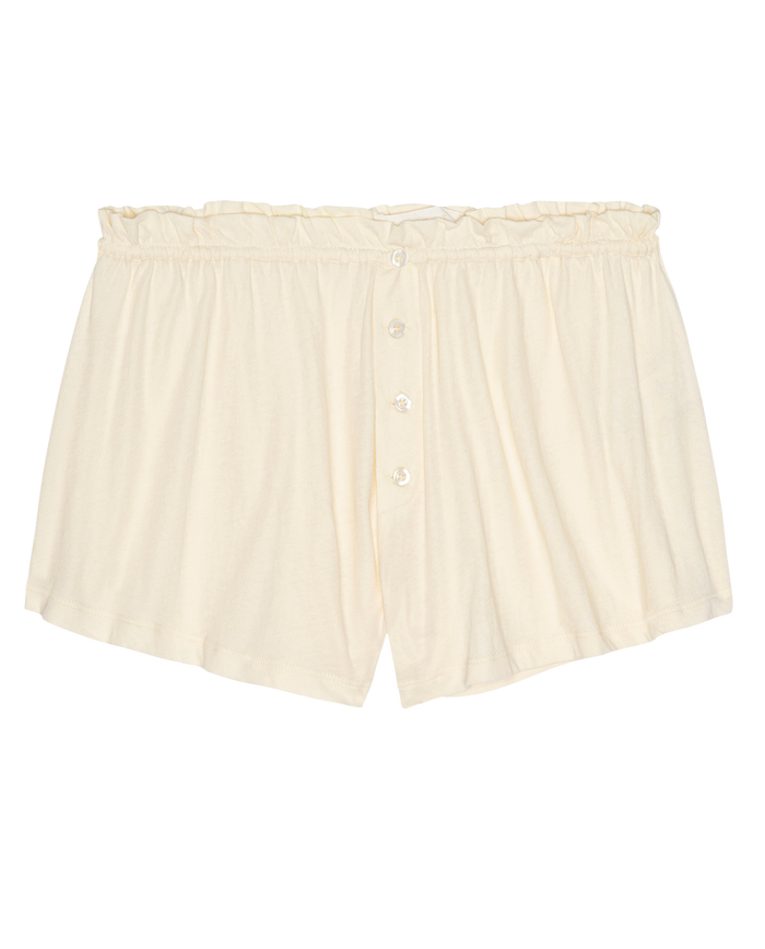 The Tap Short.. by THE GREAT. H25 SLEEP in Washed White: cream-colored women’s sleep shorts in 100% super soft cotton jersey with button front and ruffled elastic waistband, shown laid flat on a white background.