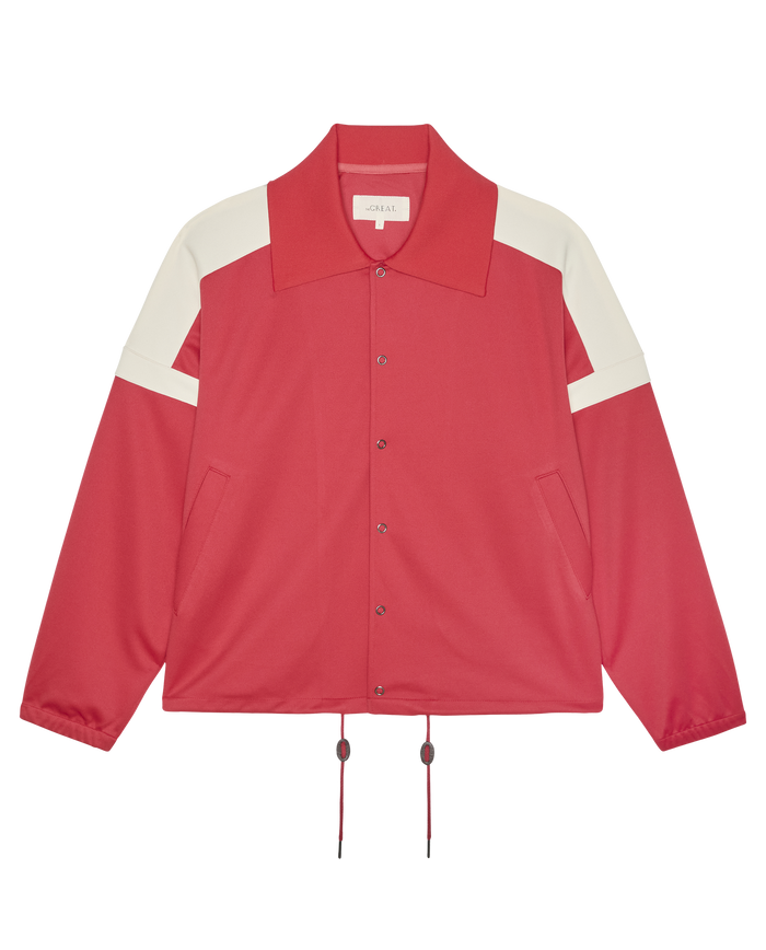 THE GREAT. SP26 D1 The Trainer Jacket in Poppy Red, featuring white shoulder stripes, a wide collar, front pockets, and adjustable hem drawstrings, laid flat on a white background.