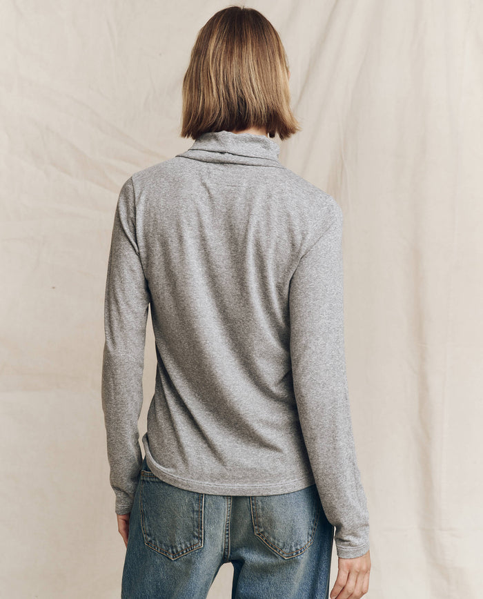 A person with shoulder-length hair is facing away, showcasing "The Turtleneck" in Heather Grey by THE GREAT. HOL 24 TURTLENECKS, paired with blue jeans, making a subtle fashion statement.