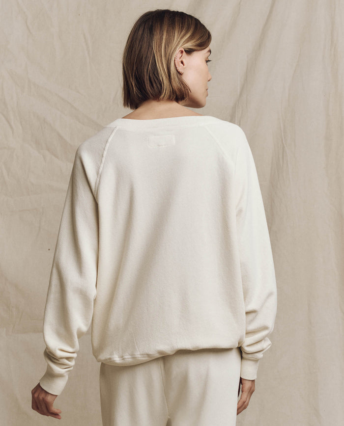 A person with short hair is turned away from the camera, wearing THE GREAT. FALL 24 KNITS' The V-Neck Sweatshirt in Washed White and matching pants against a neutral background.