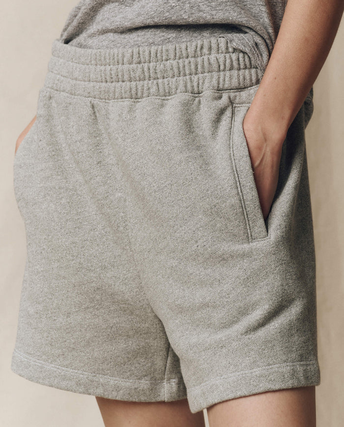 Someone wearing THE GREAT. SU25 CORE KNITS The Victory Short. Solid in Varsity Grey, featuring an elastic waistband and side pockets—ideal for performance and comfort for fans of athletic shorts.
