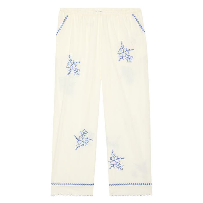 THE GREAT. SP26 D2’s The Weekend Pant W/ Hanky Embroidery in cream features blue hanky embroidery, a scalloped hem, and an elastic waistband, shown flat on a white background.
