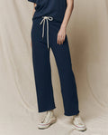 A person wearing The Wide Leg Cropped Sweatpant in True Navy, by THE GREAT. FALL 23 KNITS, features a drawstring waist and wide cropped legs, perfectly paired with white high-top sneakers. These 100% cotton pants offer stylish comfort and easy elegance.