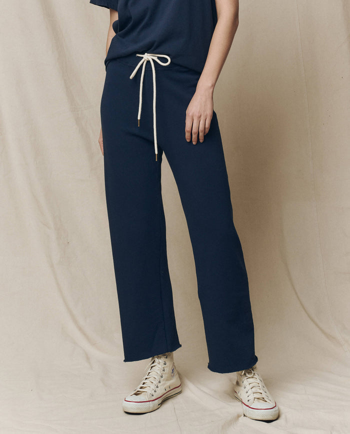 A person wearing The Wide Leg Cropped Sweatpant in True Navy, by THE GREAT. FALL 23 KNITS, features a drawstring waist and wide cropped legs, perfectly paired with white high-top sneakers. These 100% cotton pants offer stylish comfort and easy elegance.
