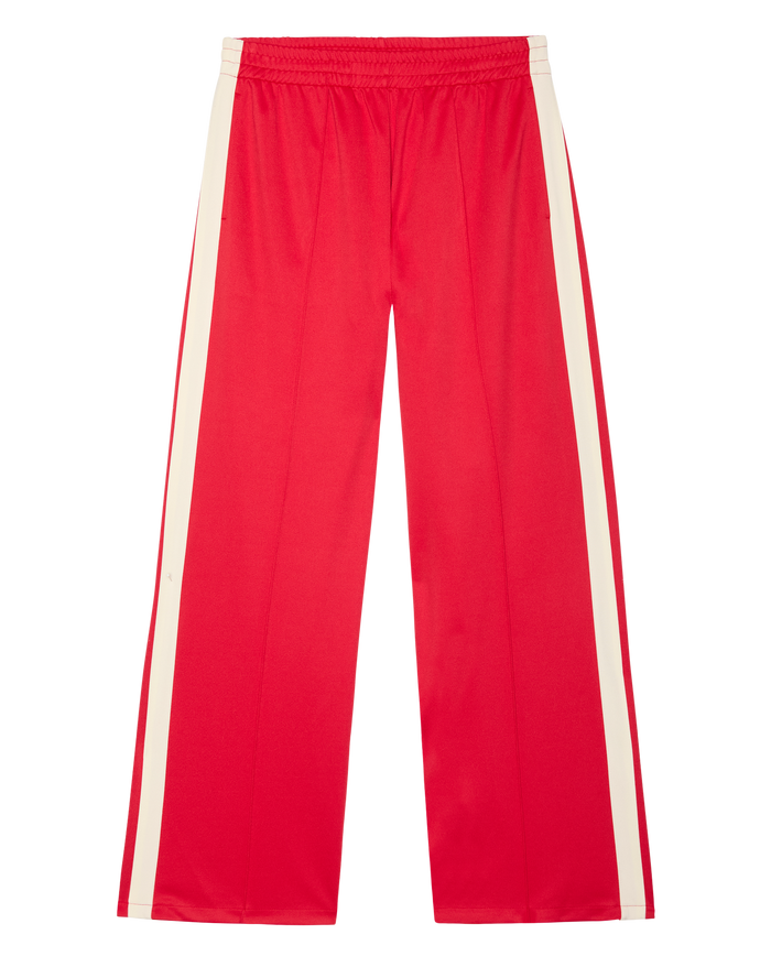 THE GREAT. SP26 D1 The Wide Leg Track Pant in Poppy Red features a roomy wide-leg silhouette, crisp white side stripes, and an elastic waistband, shown on a white background.