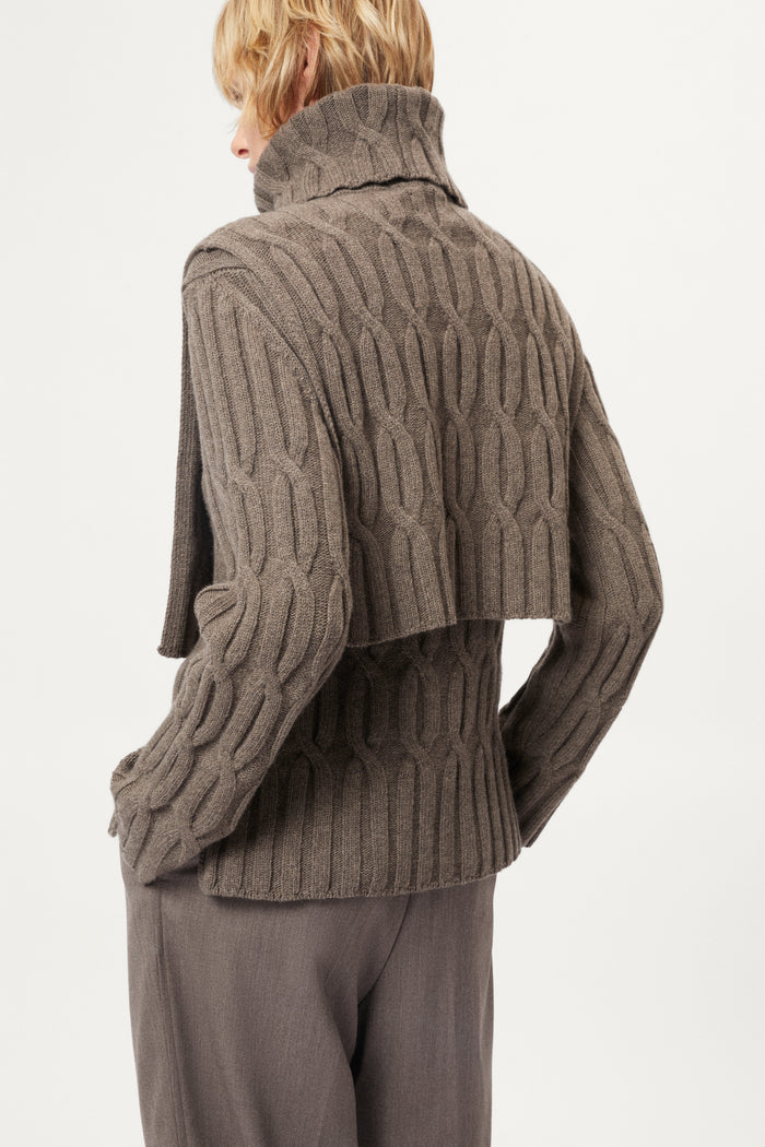 Woman wearing a brown cable knit bib and pants on a white background