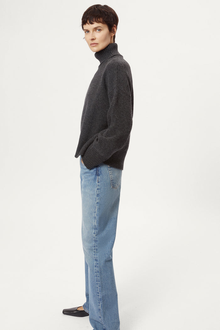 woman wearing a woolen dark grey turtleneck sweater and blue jeans on a white background