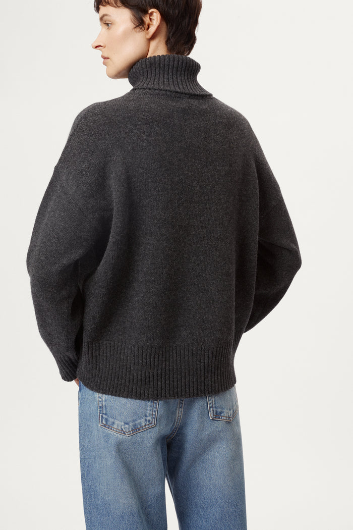 woman wearing a woolen dark grey turtleneck sweater and blue jeans on a white background