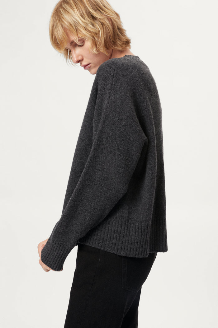 Woman wearing a woolen dark gray sweater and black pants on a white background