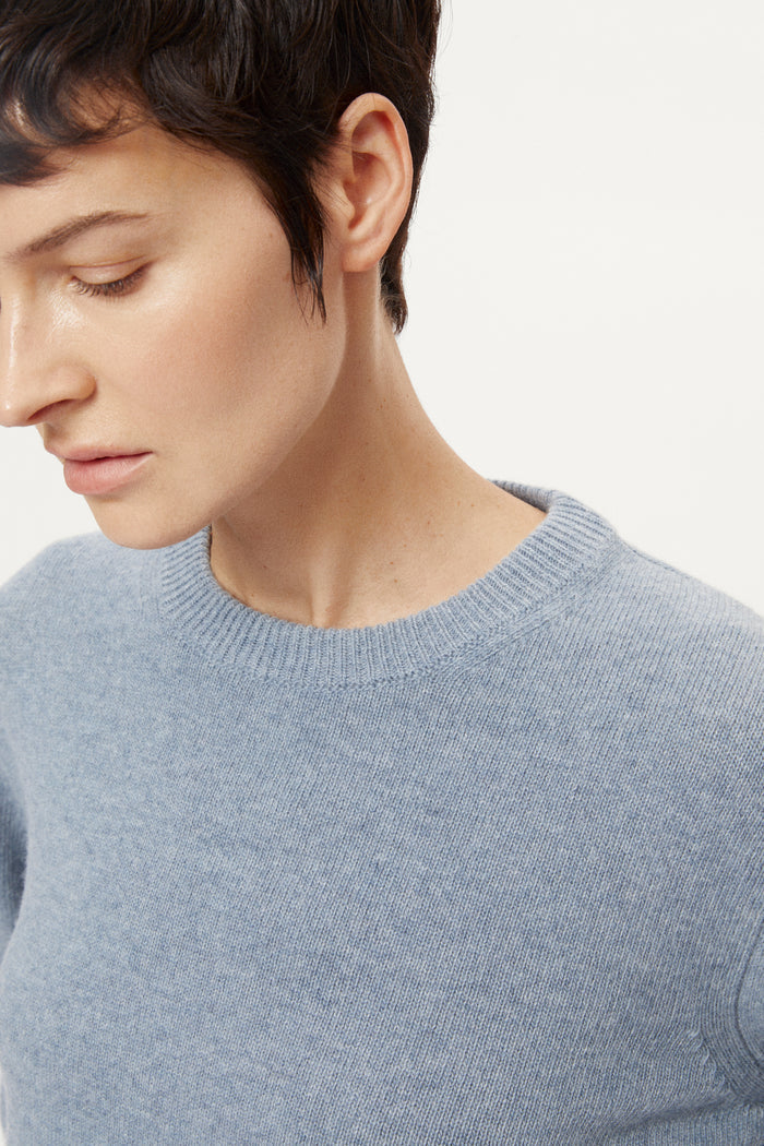 woman wearing a woolen light blue sweater and dark pants on a white background