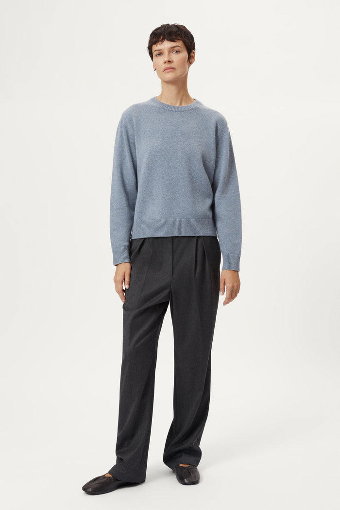 woman wearing a woolen light blue sweater and dark pants on a white background