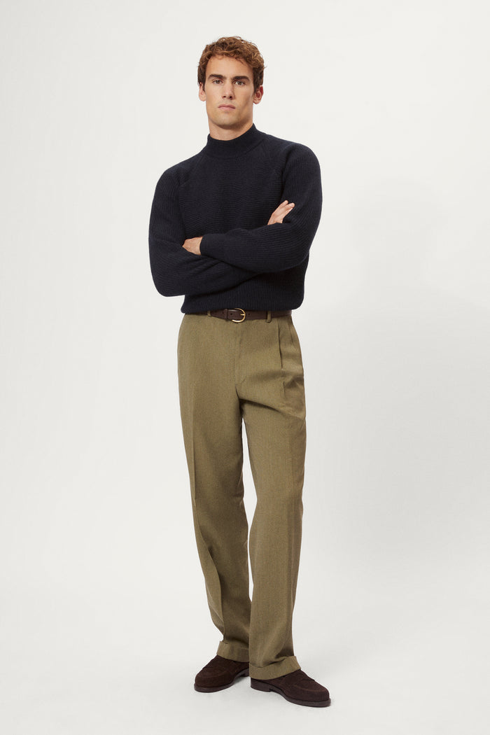 Man wearing a dark blue woolen ribbed sweater and green pants on a white background