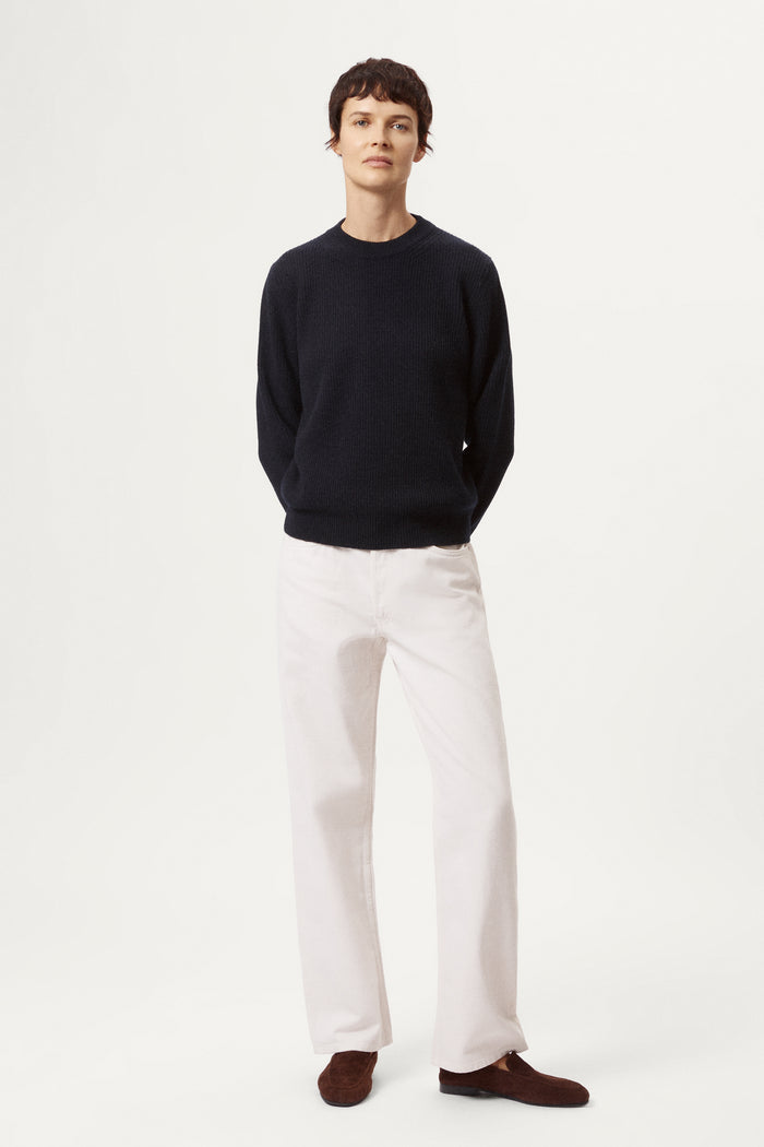 woman wearing a blue navy woolen sweater and white pants against a light background