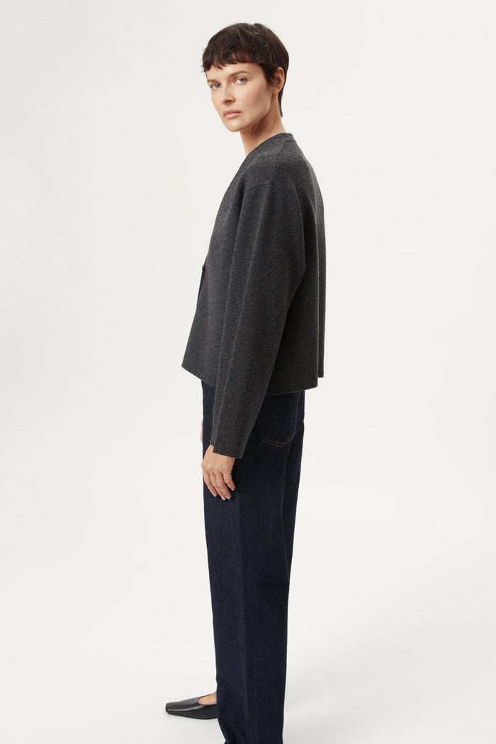 woman wearing a woolen dark gray cardigan with dark jeans on a white background