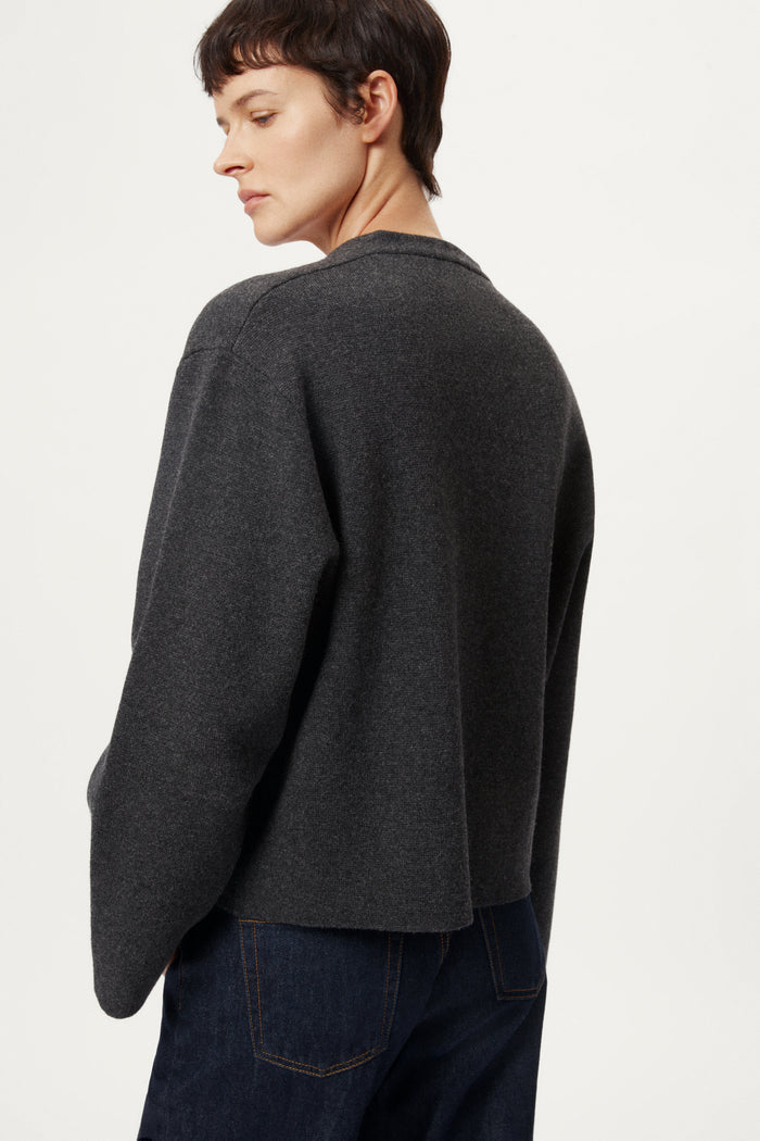 woman wearing a woolen dark gray cardigan with dark jeans on a white background