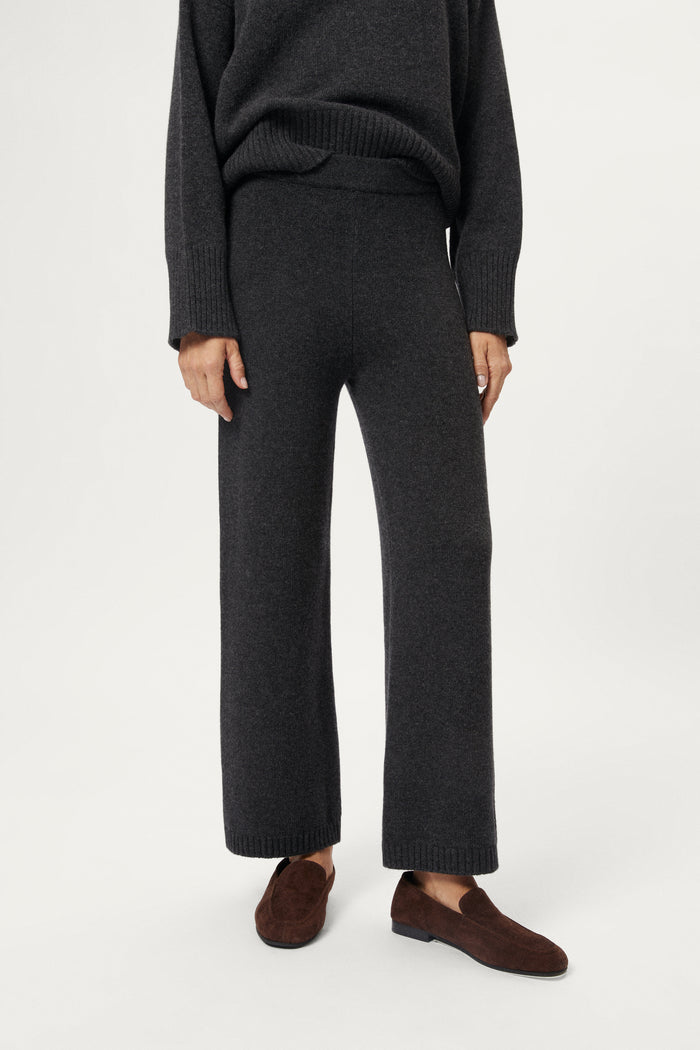 Woman wearing a woolen dark gray sweater and pants with brown shoes on a white background