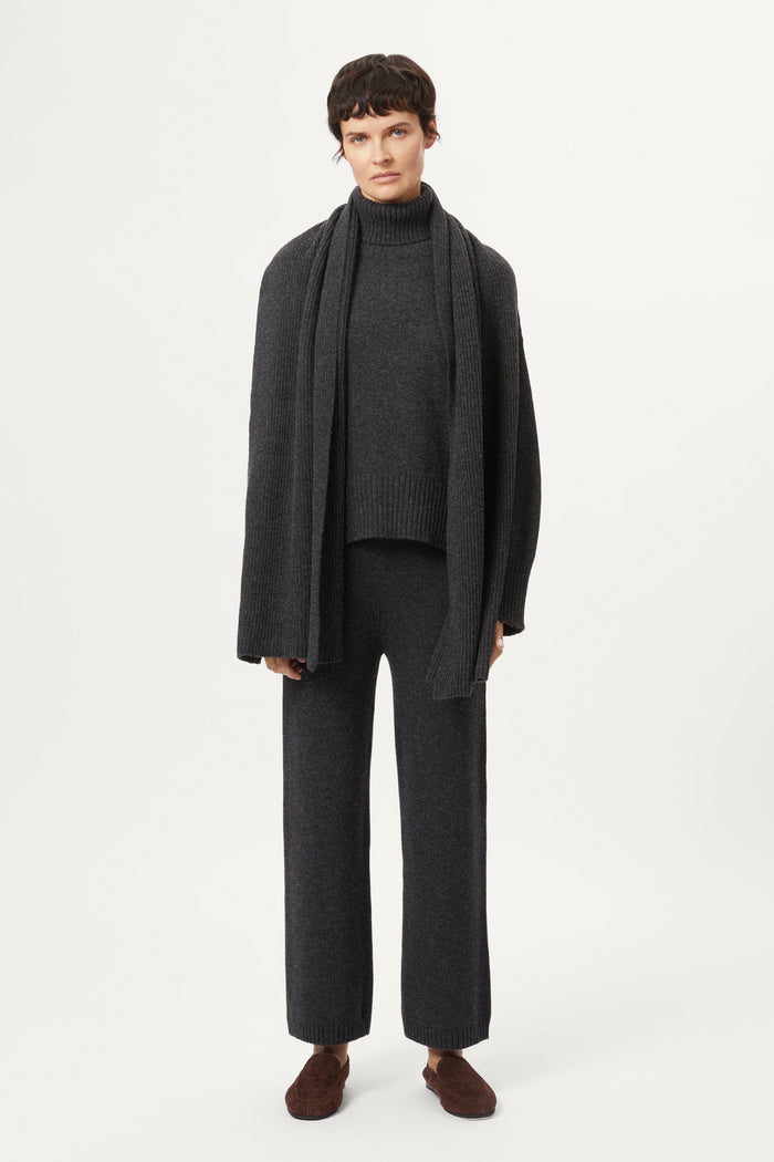 Woman wearing a woolen dark gray sweater and pants with brown shoes on a white background