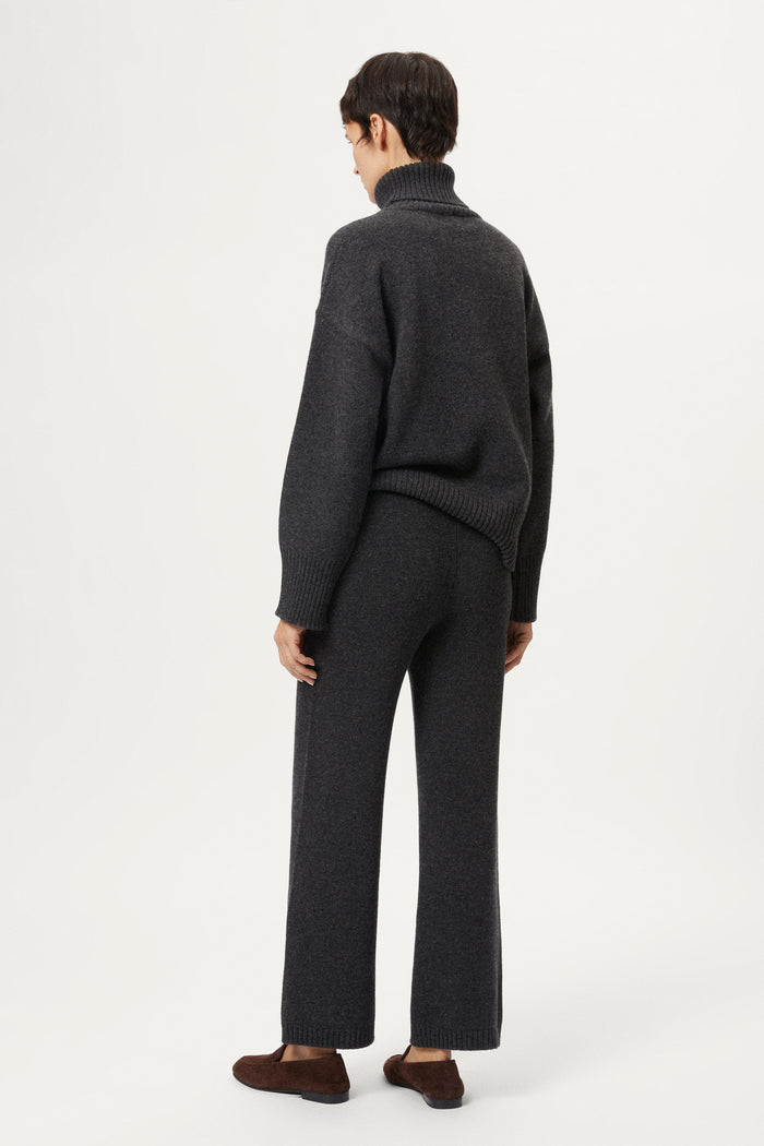 Woman wearing a woolen dark gray sweater and pants with brown shoes on a white background