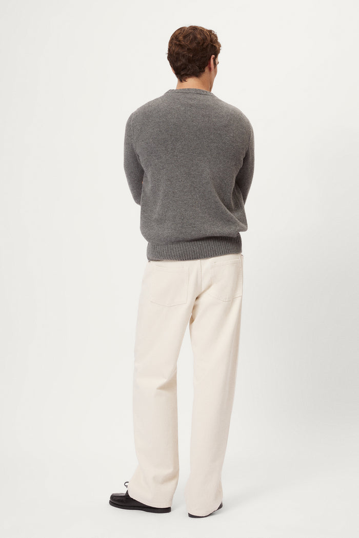 Man wearing a gray woolen sweater and white pants against a white background