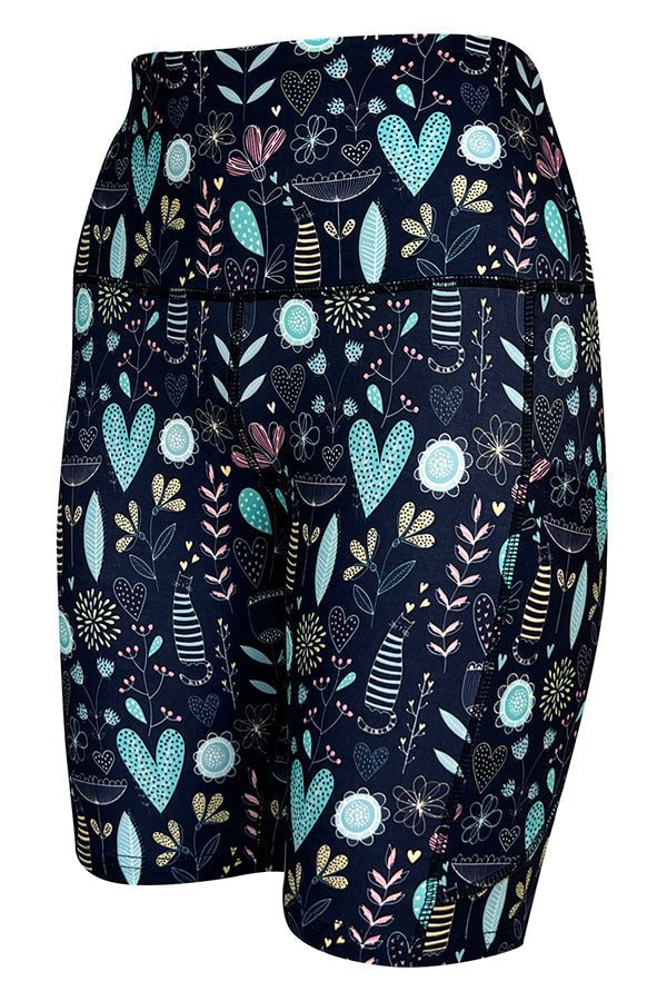 Wildflower Whiskers Shorts with floral, heart, and striped kitty patterns in pastel colors on blue, featuring deep side pockets and structured stitching.