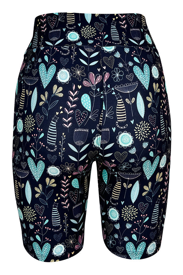 Black tight shorts with pastel floral, heart, and striped cat pattern on a blue background.